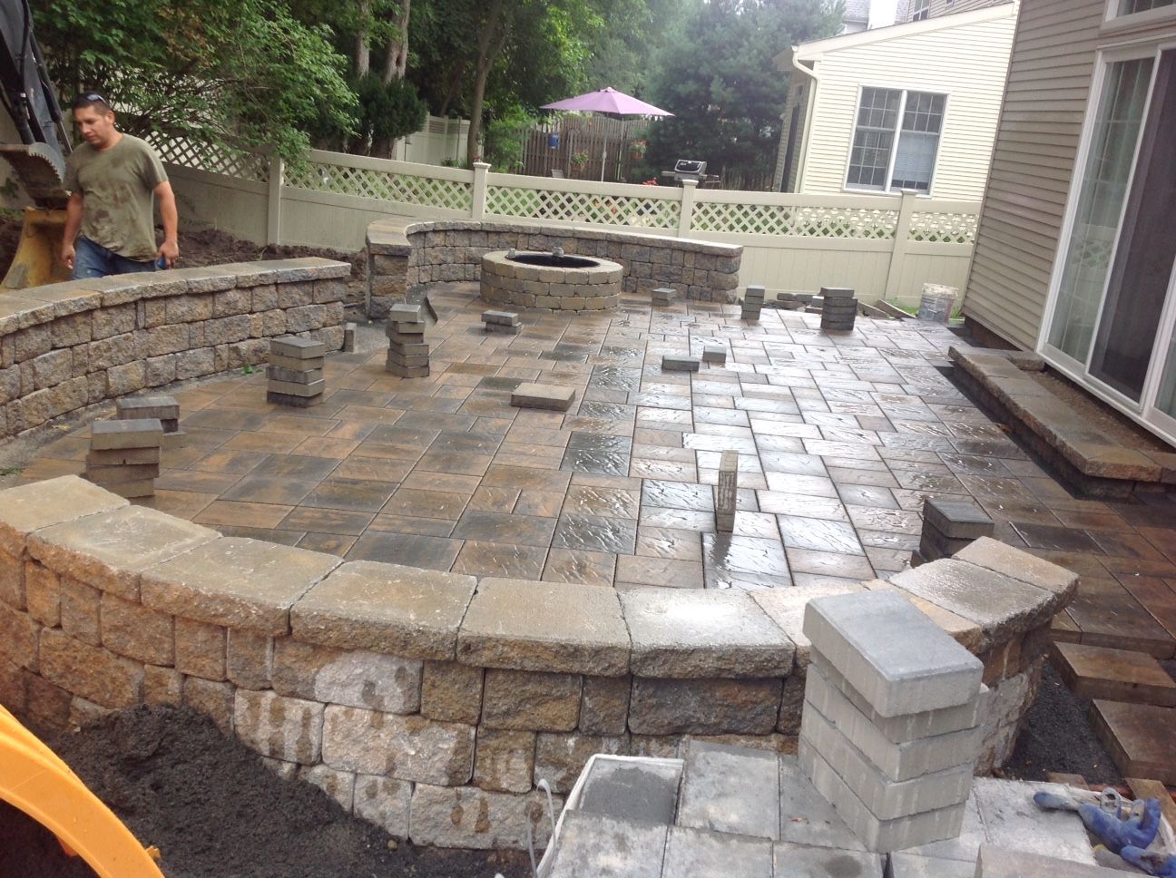 A man is working on a patio with a fire pit in the middle of it.