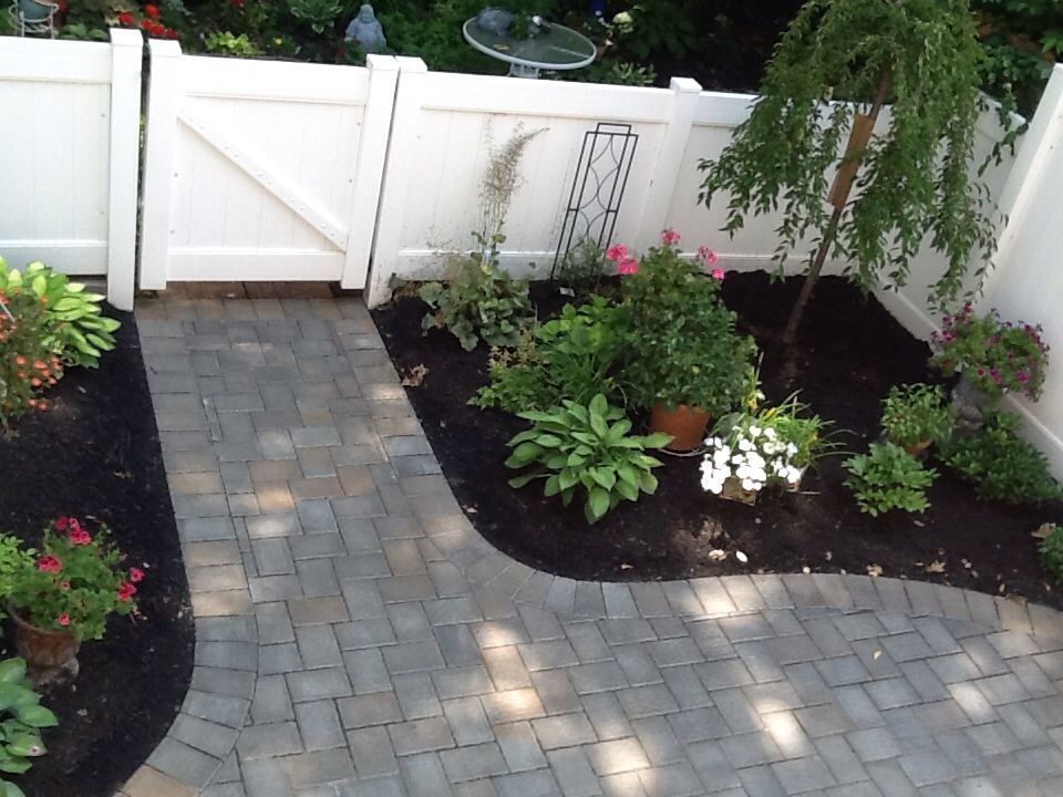 A white fence surrounds a garden with flowers and plants