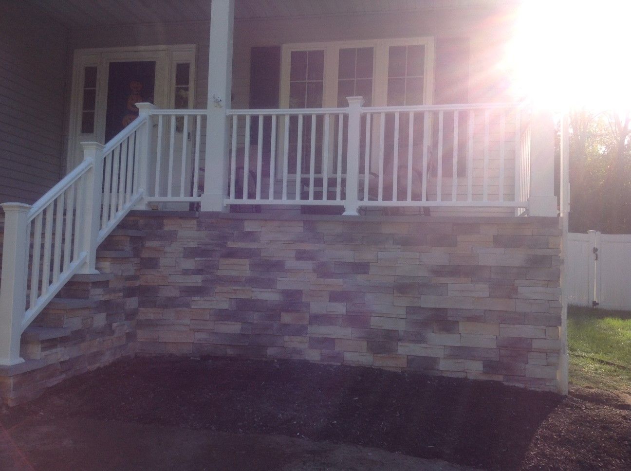 A porch with a white railing and stairs is lit up at night.