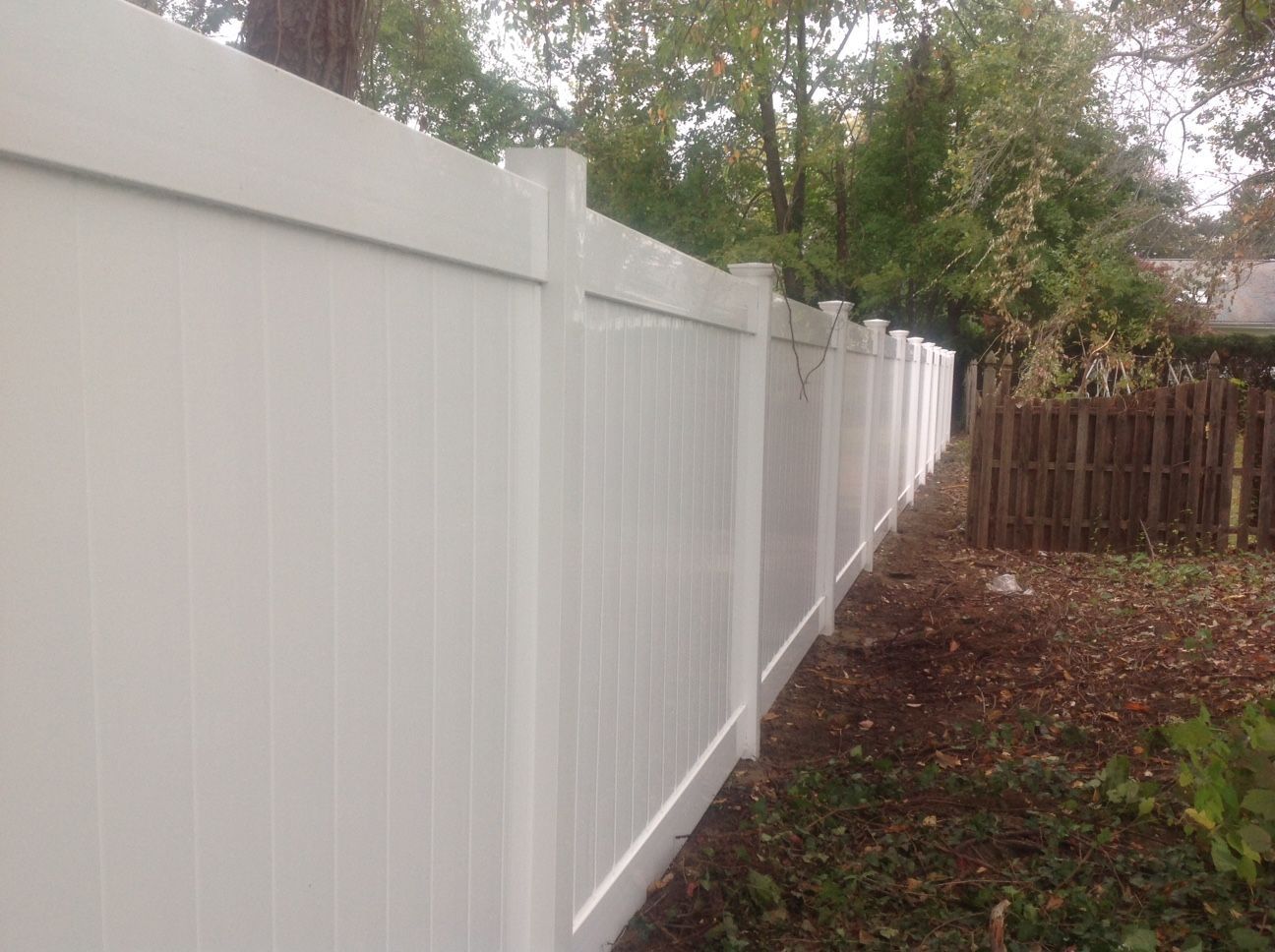 A white vinyl fence is surrounded by trees in a backyard.