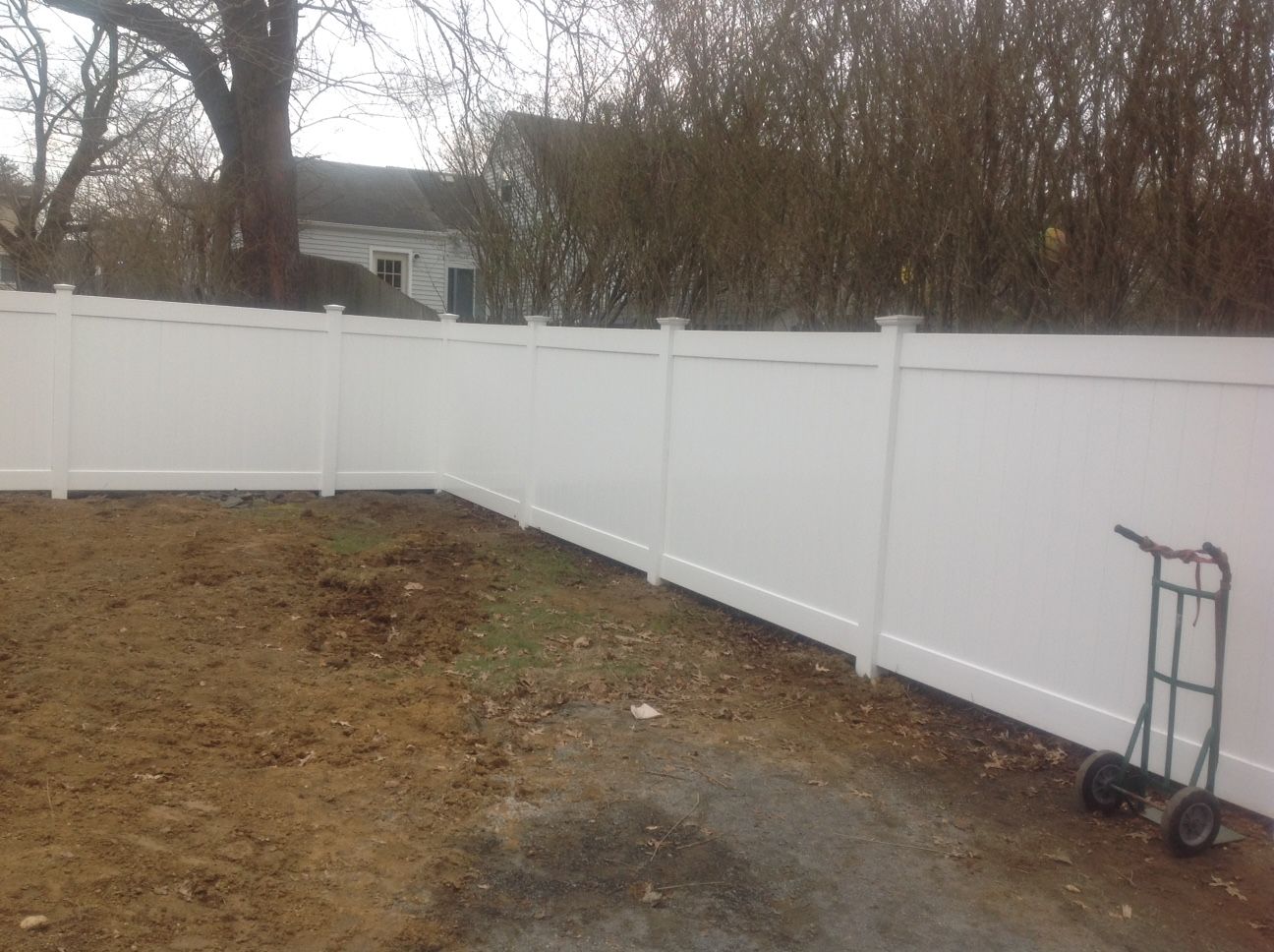 A white fence with a dolly in front of it in a backyard.