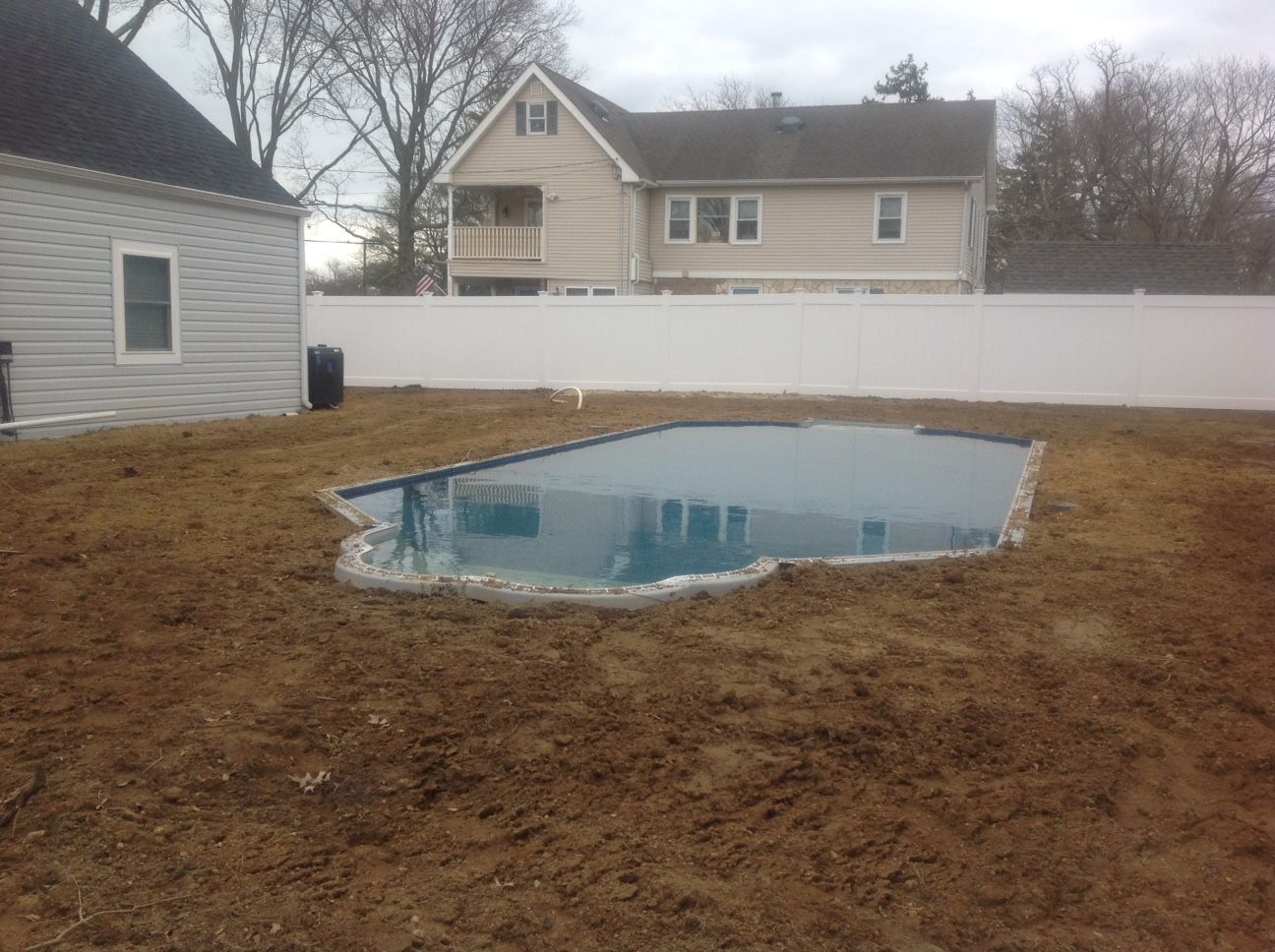 A large swimming pool is sitting in the middle of a backyard next to a house.