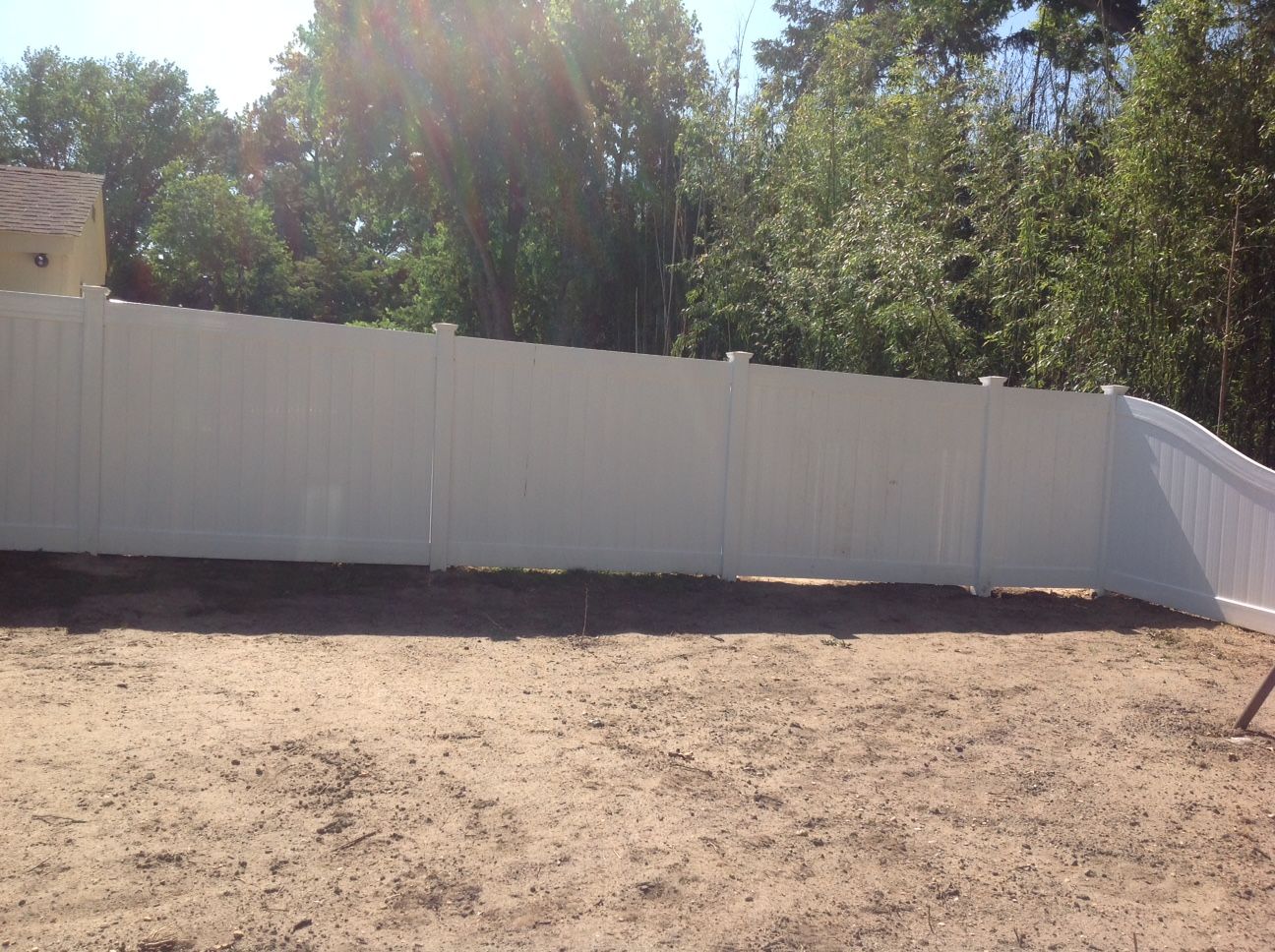 A white fence surrounds a dirt field with trees in the background.