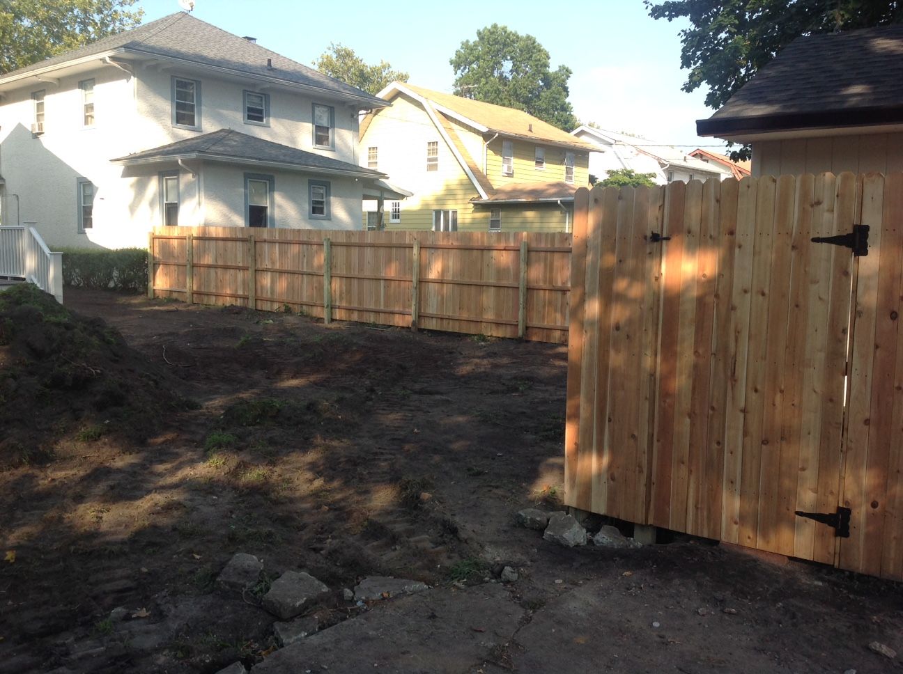 A wooden fence surrounds a dirt area in front of a house