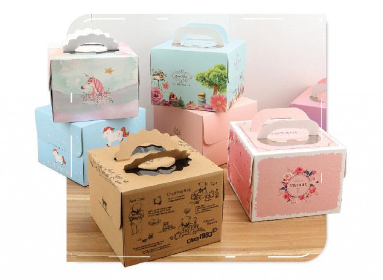 Colorful, decorative cake boxes with handles in various designs, stacked on a wooden surface.