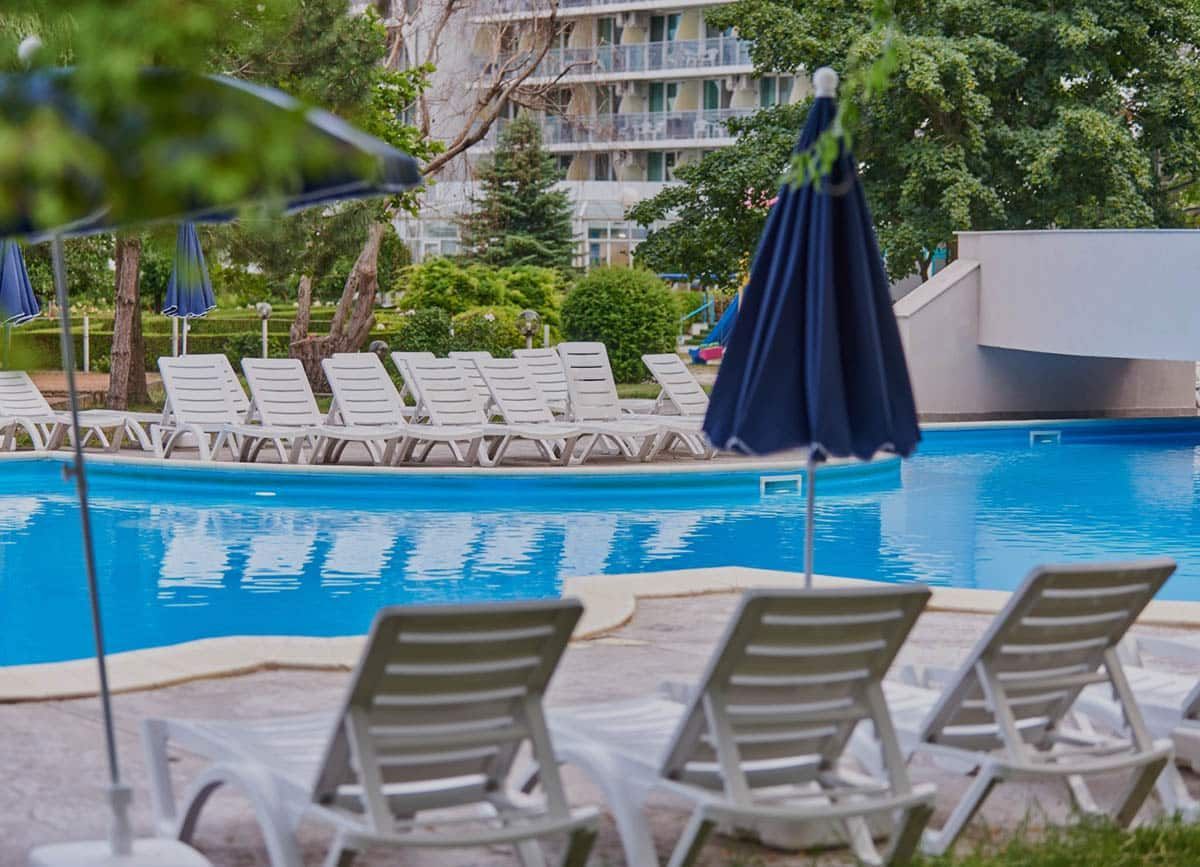 A pool with white lounge chairs and a closed navy umbrella, near a building.