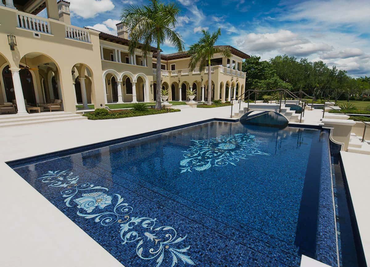 A luxurious mansion with a large, blue-tiled swimming pool featuring decorative mosaic designs.