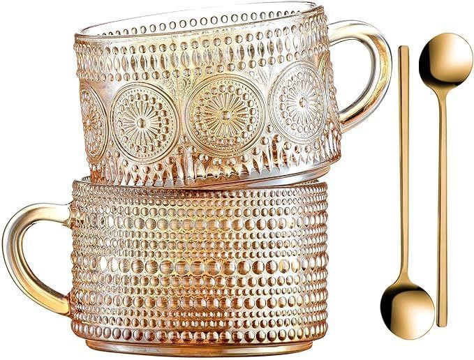 two glass mugs with gold handles and spoons on a white background .