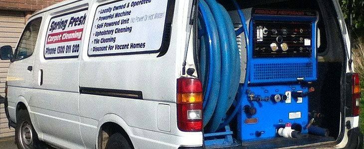 A white van with a blue machine in the back is parked in a driveway.