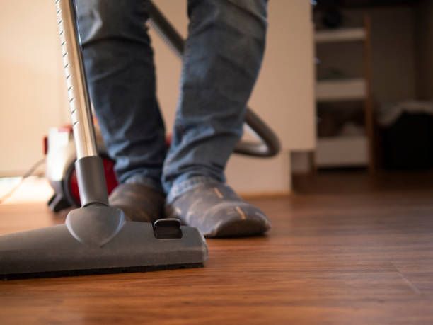 A person is using a vacuum cleaner on a wooden floor.