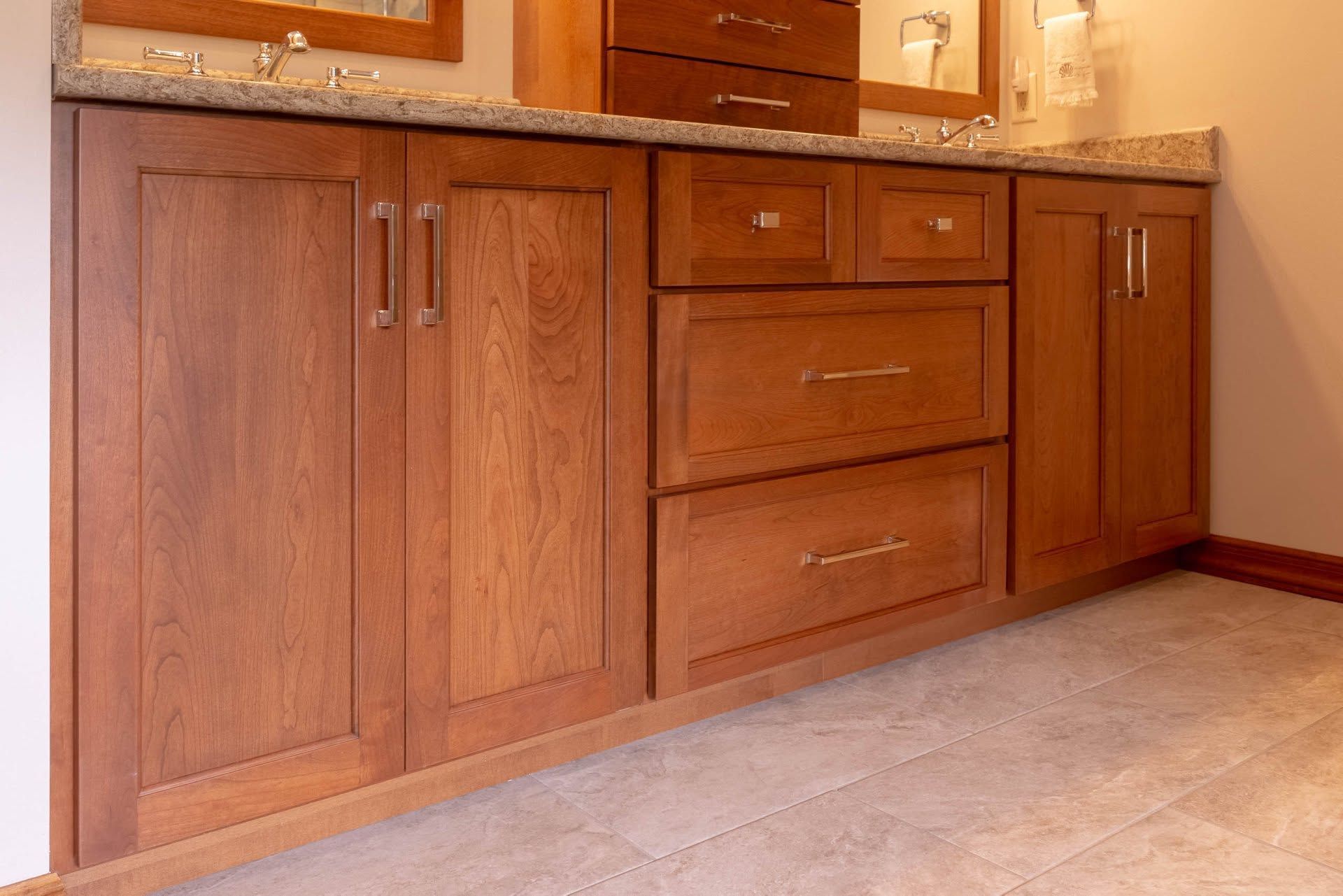 Wooden bathroom vanity with cabinet doors and drawers beside a beige countertop and sink.