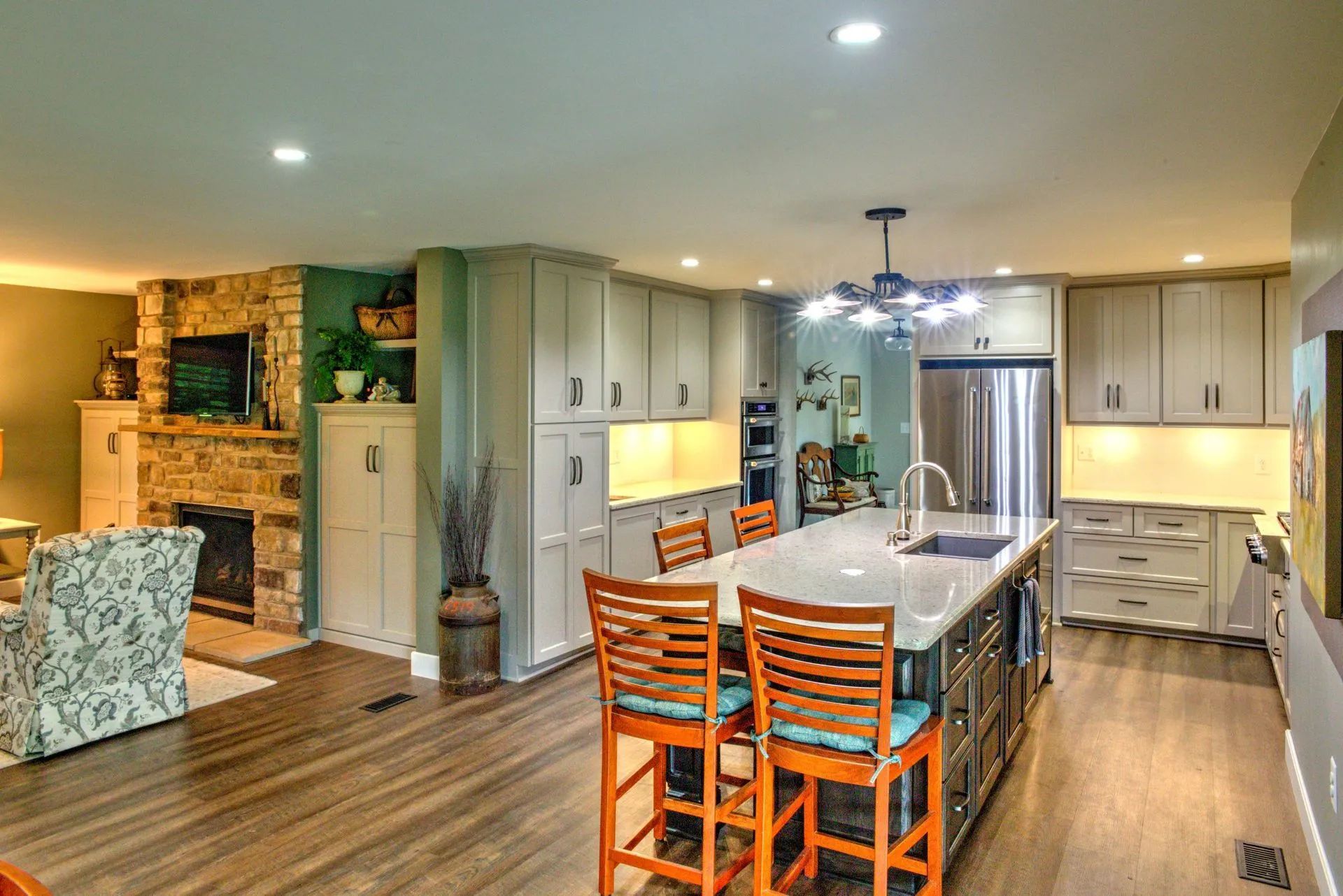 Modern kitchen with island, cabinets, and fireplace. Wood floors, orange bar stools, and stainless steel appliances.