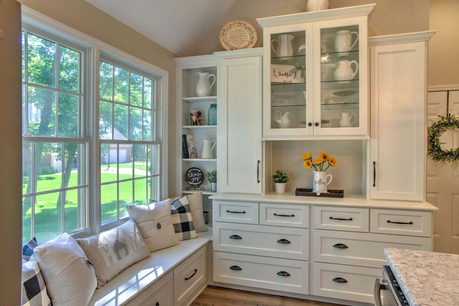 White kitchen cabinetry with a built-in window seat and glass-front display cabinet.