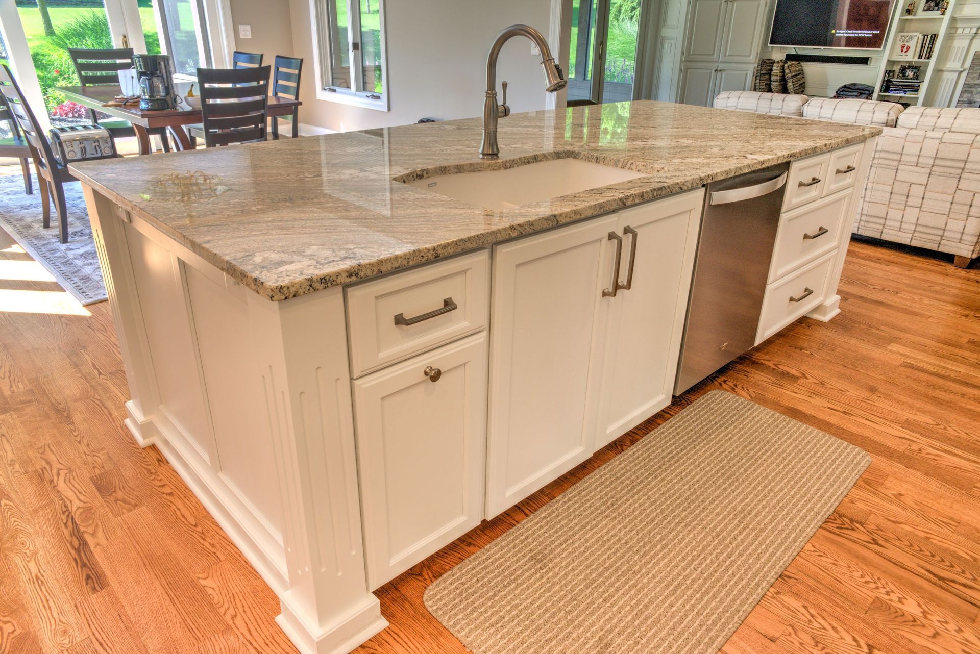 Kitchen island with granite countertop, white cabinets, and stainless steel faucet and dishwasher.
