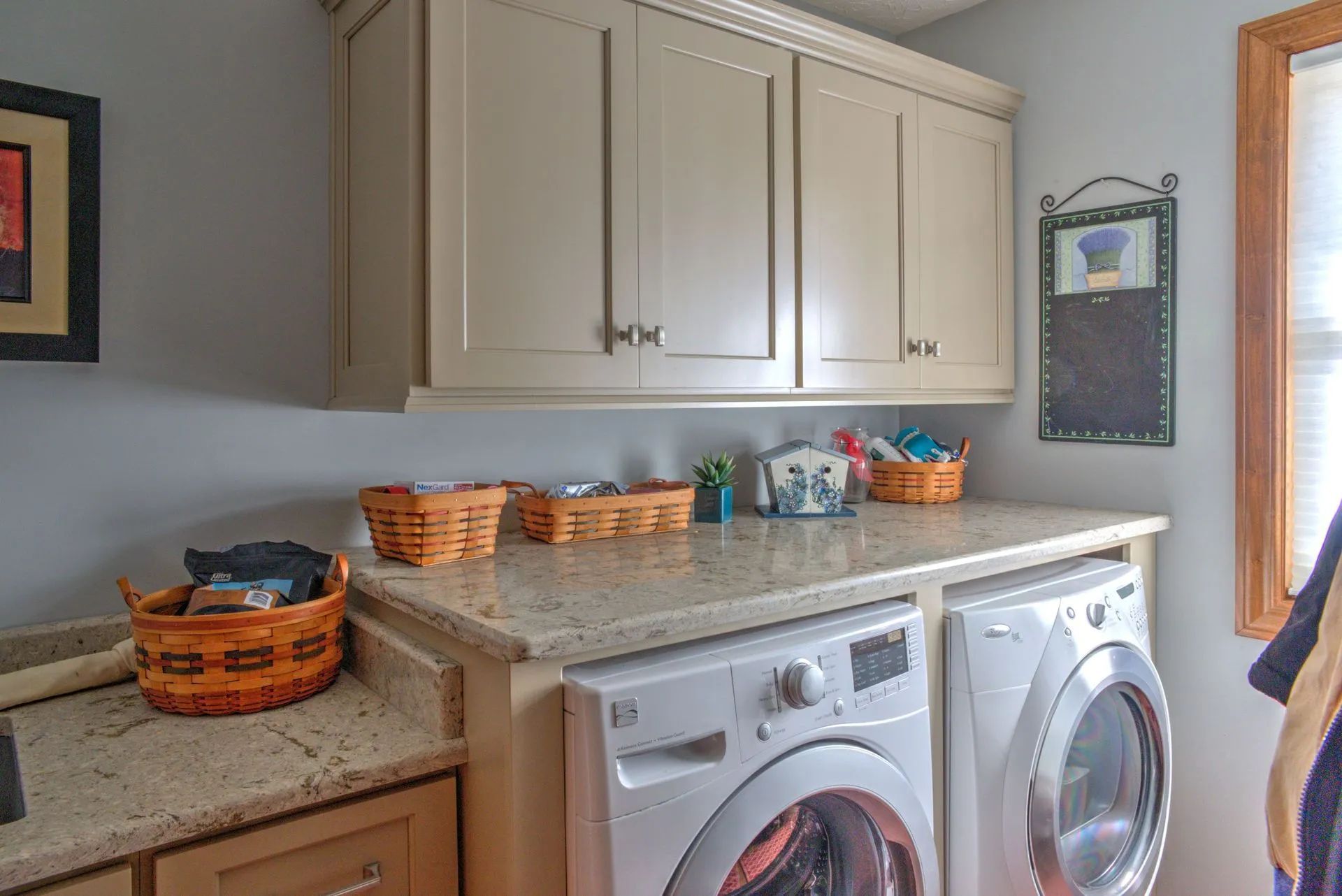 Laundry room with cream cabinets, granite countertop, washer and dryer. Baskets and a chalkboard.