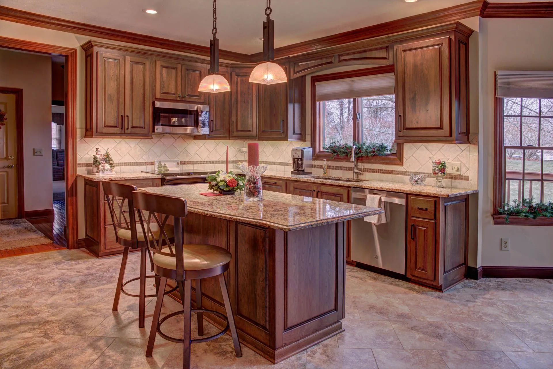 Kitchen with brown cabinets, granite countertops, island with stools, and windows.