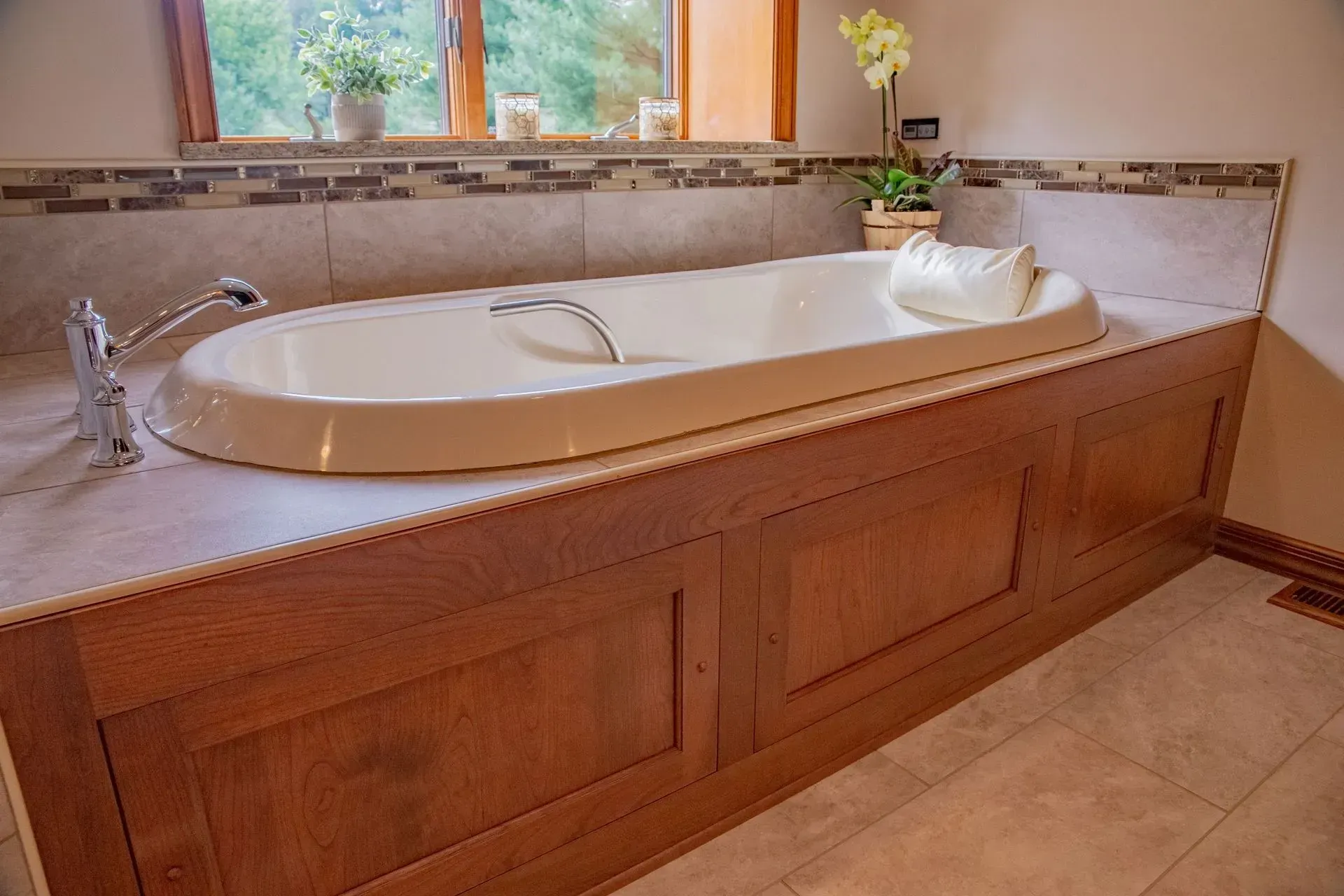 A bathtub in a bathroom with wooden cabinets and a window.