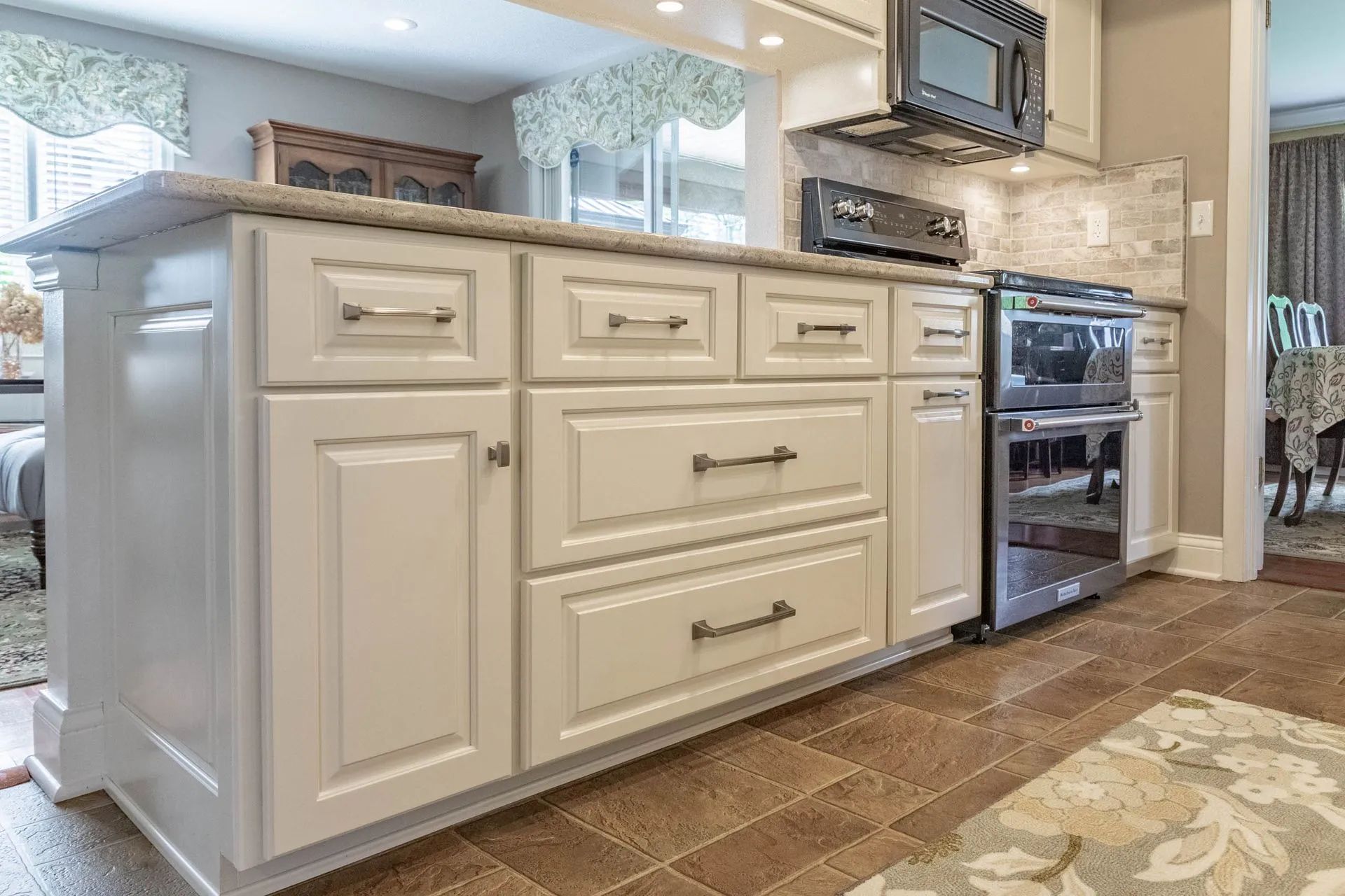 Off-white kitchen cabinets and an island with stainless steel appliances set against a tiled floor and neutral walls.