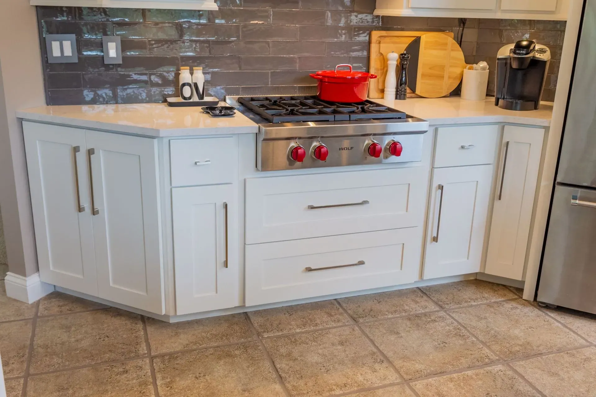 A kitchen with white cabinets , stainless steel appliances , and a red pot on the stove.