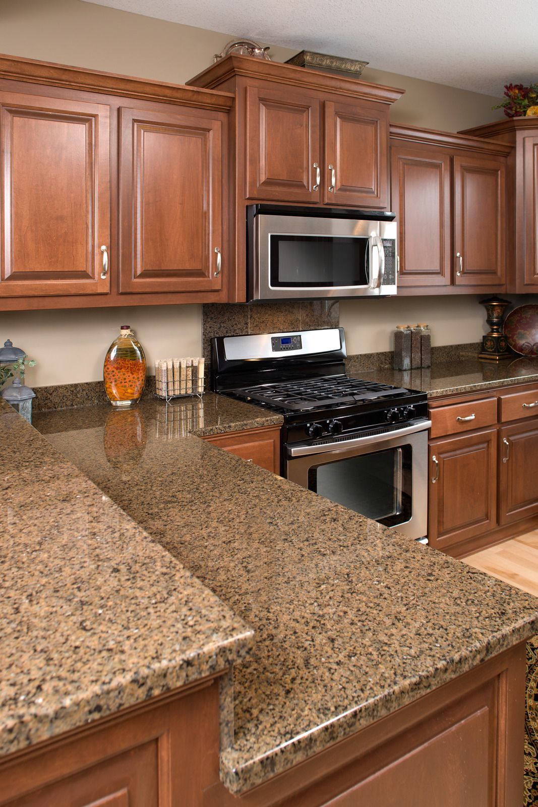 A kitchen with wooden cabinets , granite counter tops , a stove and microwave.