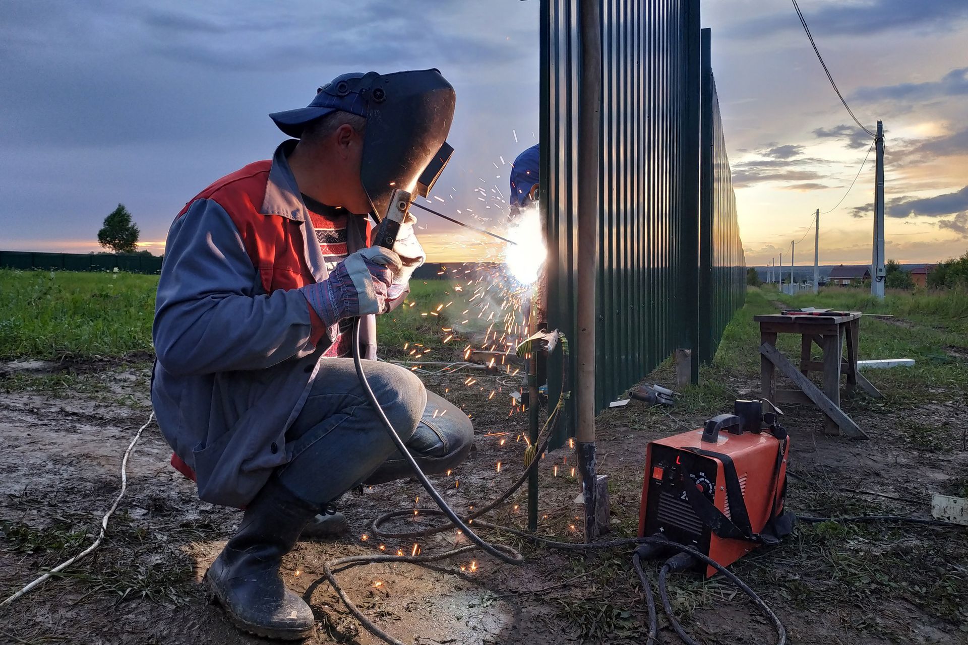 A man is welding a metal fence in a field.