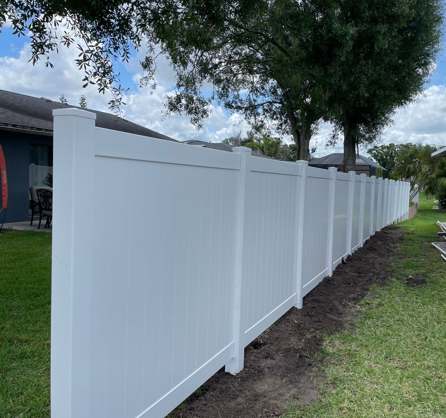 A white fence is surrounded by trees and grass in front of a house.