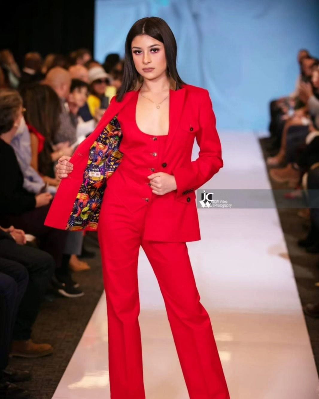 A woman in a red suit is walking down a runway at a fashion show.
