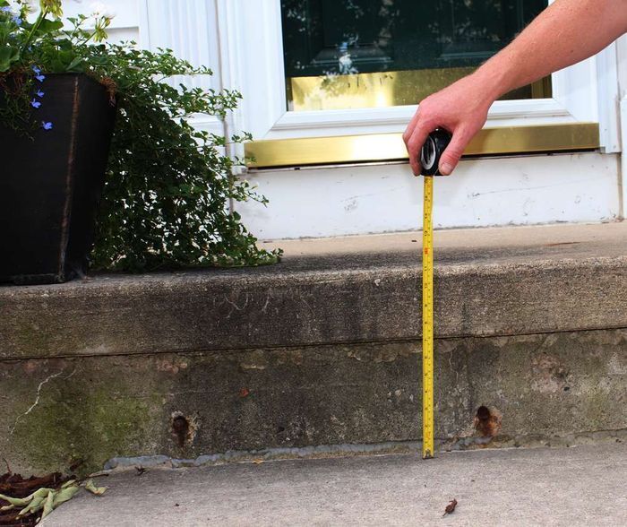 Person measuring a concrete step with a yellow tape measure.