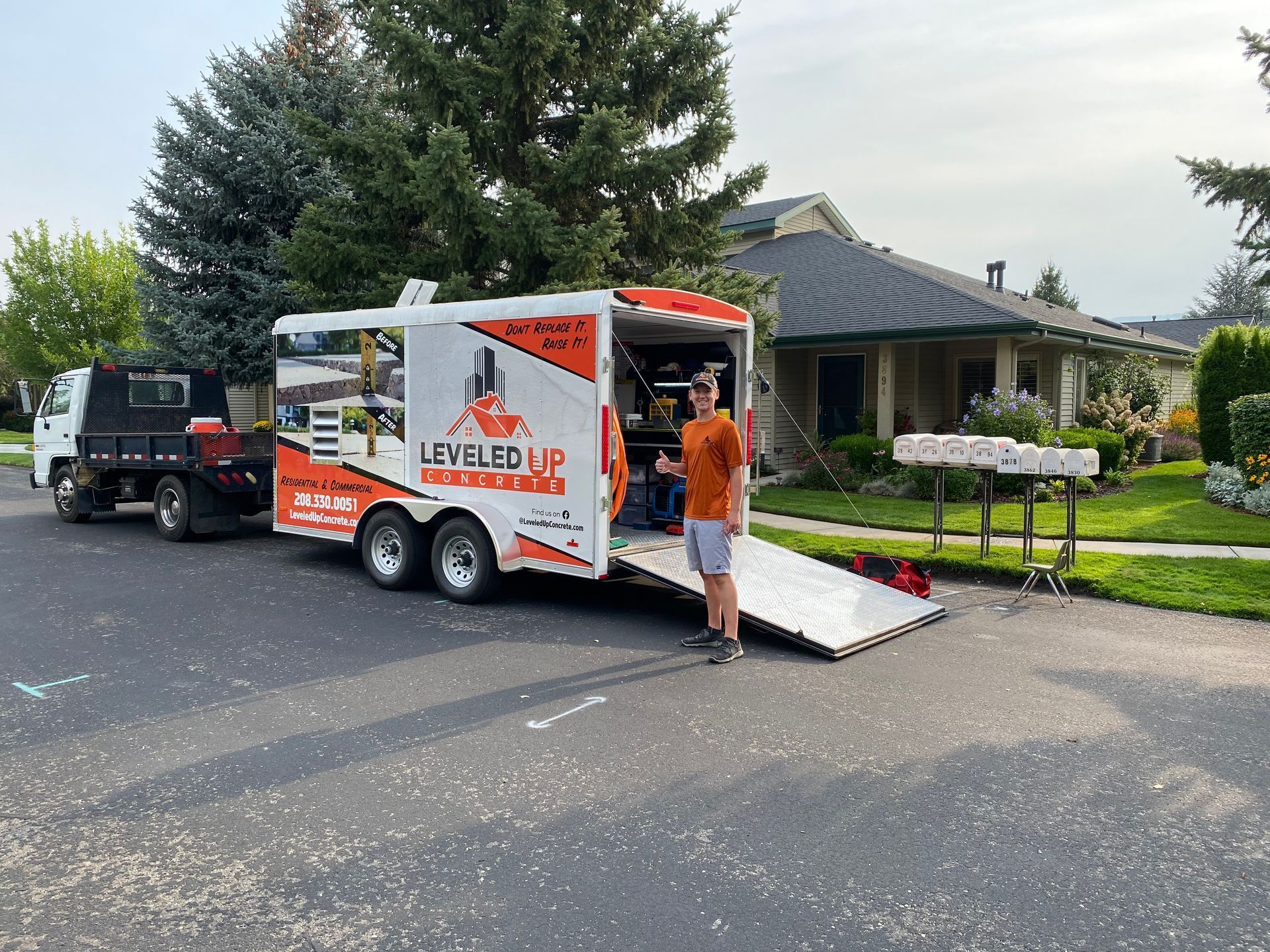 Man stands by a moving trailer in a residential street. The trailer is orange and white and hitched to a truck.