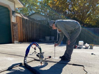 Person using a machine on concrete, repairing a crack outside a garage on a sunny day.