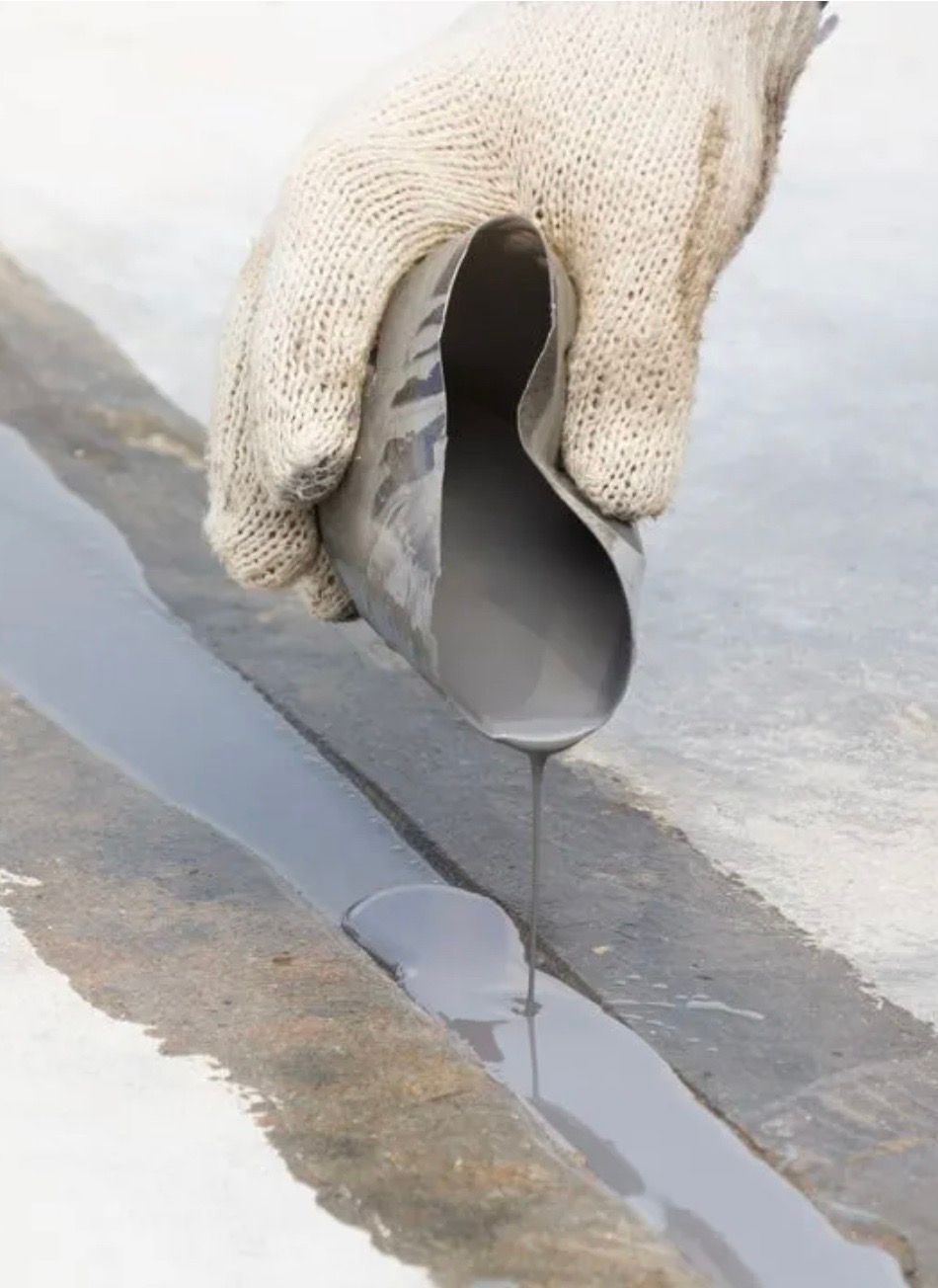 Gloved hand pouring gray sealant into a concrete crack.