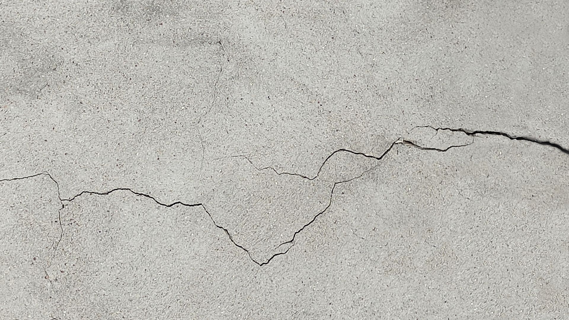 Gray concrete surface with a long, jagged black crack running across it.