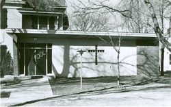 Black and white photo of a modern church with a cross-shaped window and a sign that reads