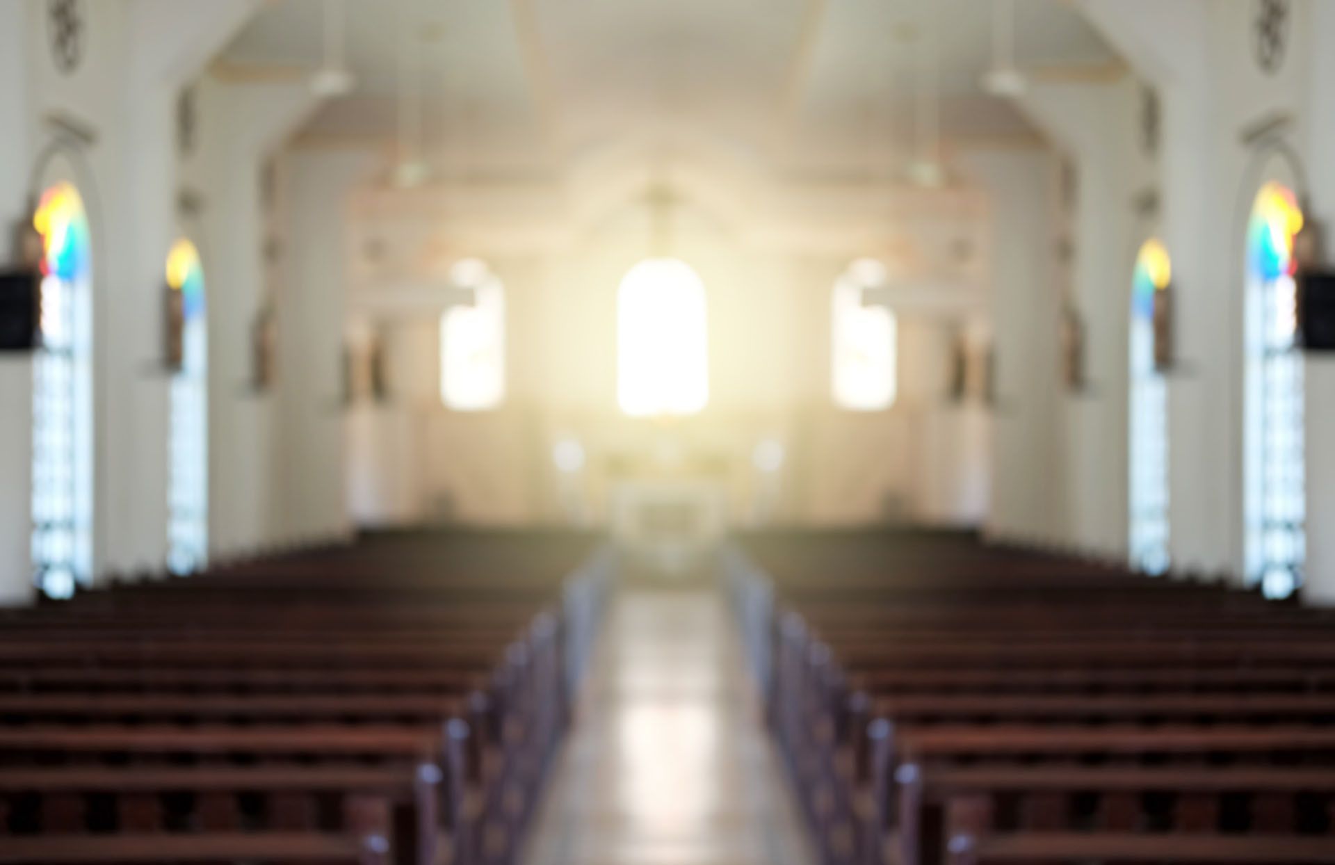 The inside of a church with rows of wooden benches and stained glass windows.