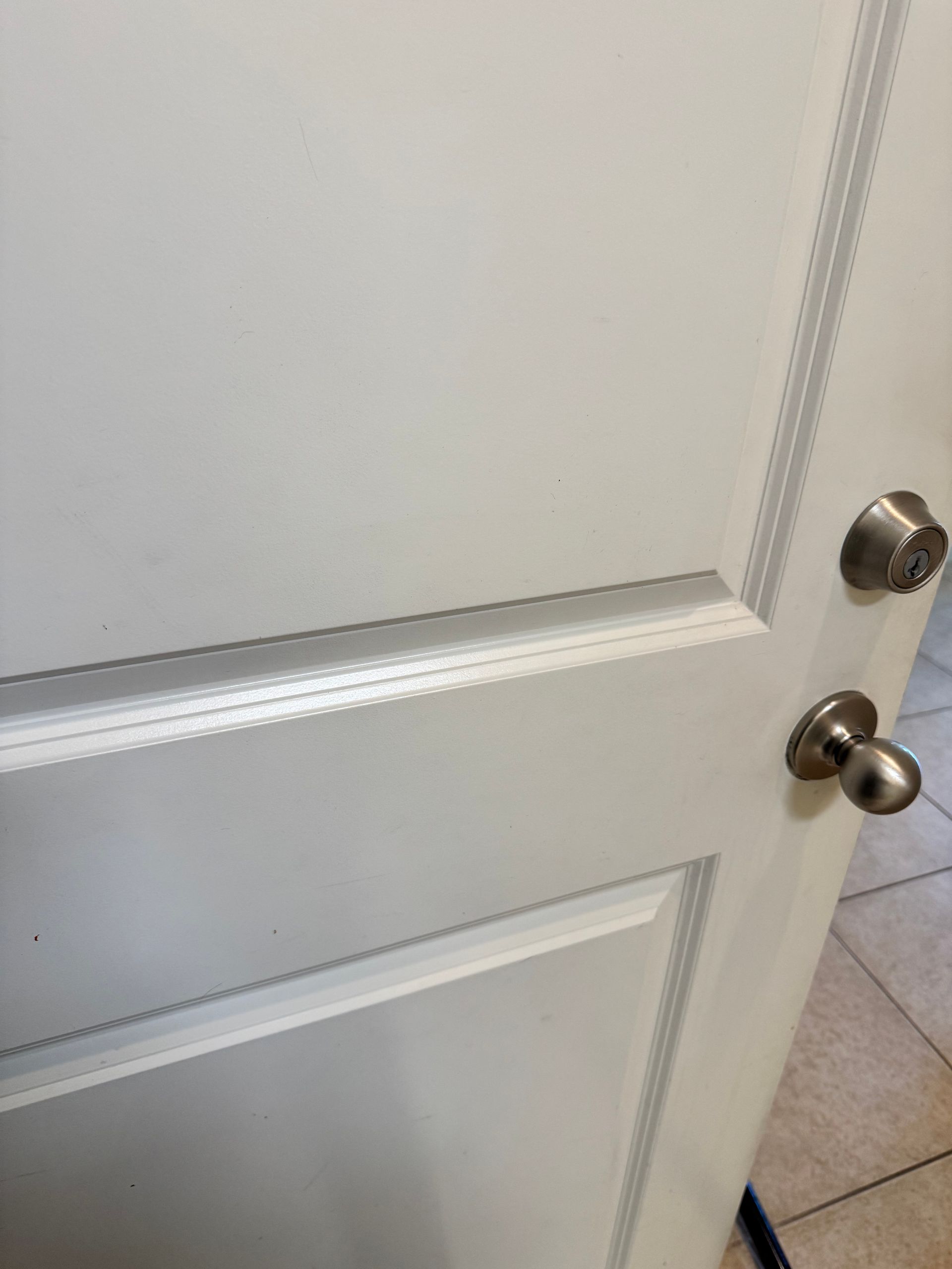 A white interior door with a brushed nickel deadbolt and matching doorknob against a tiled floor background.