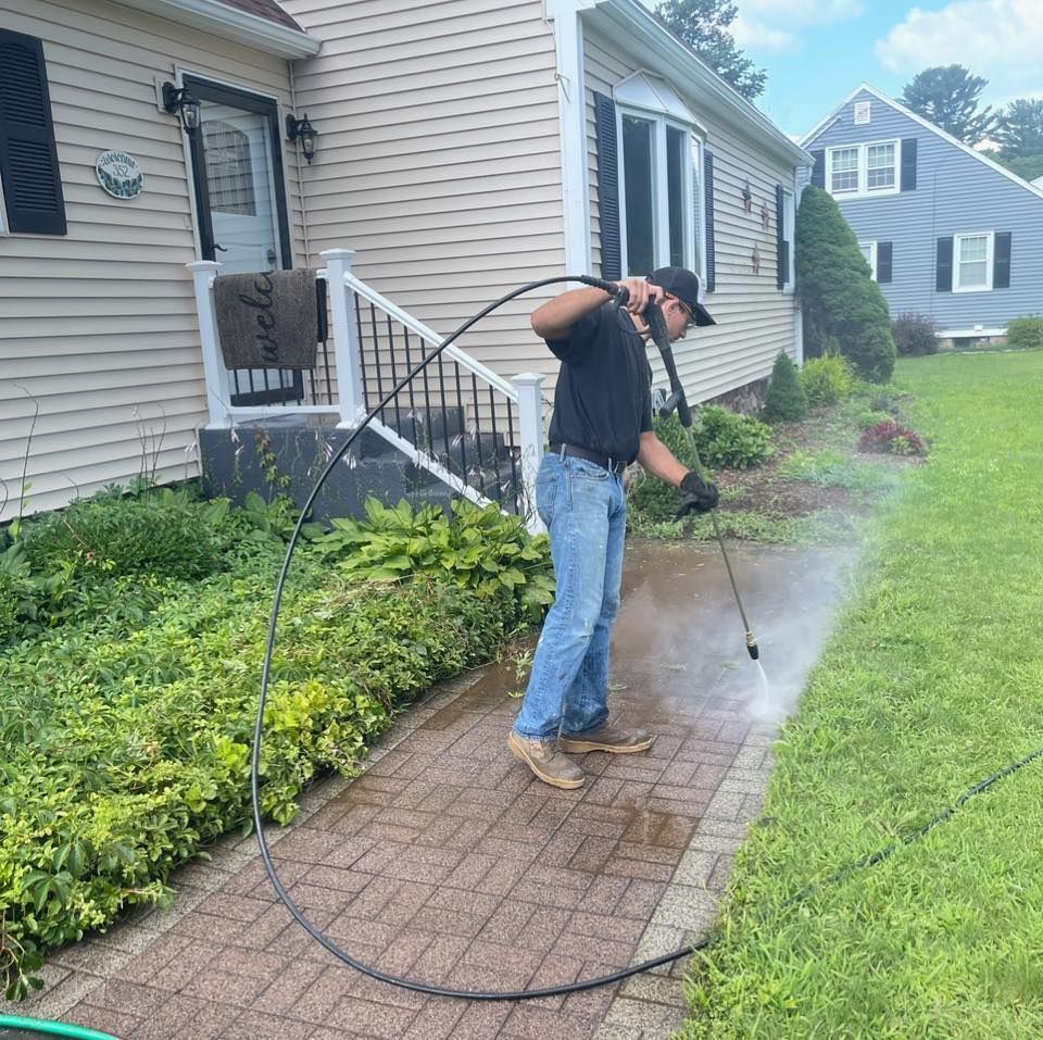 A man is using a hose to clean a sidewalk in front of a house