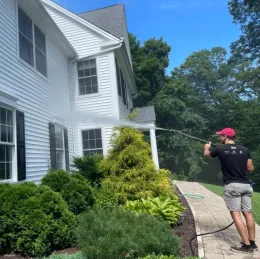 A man is using a high pressure washer to clean a white house