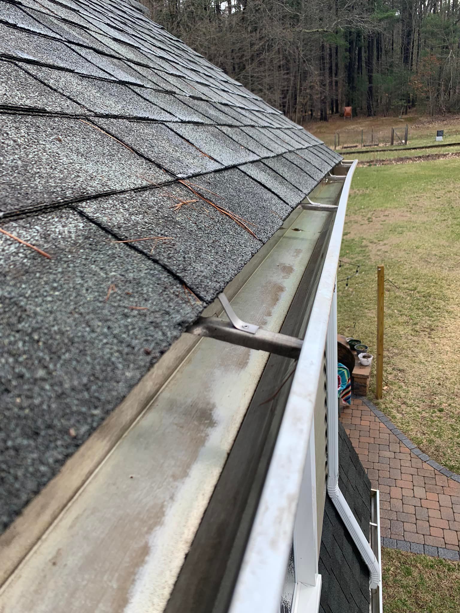 A gutter on the side of a house with a roof in the background.