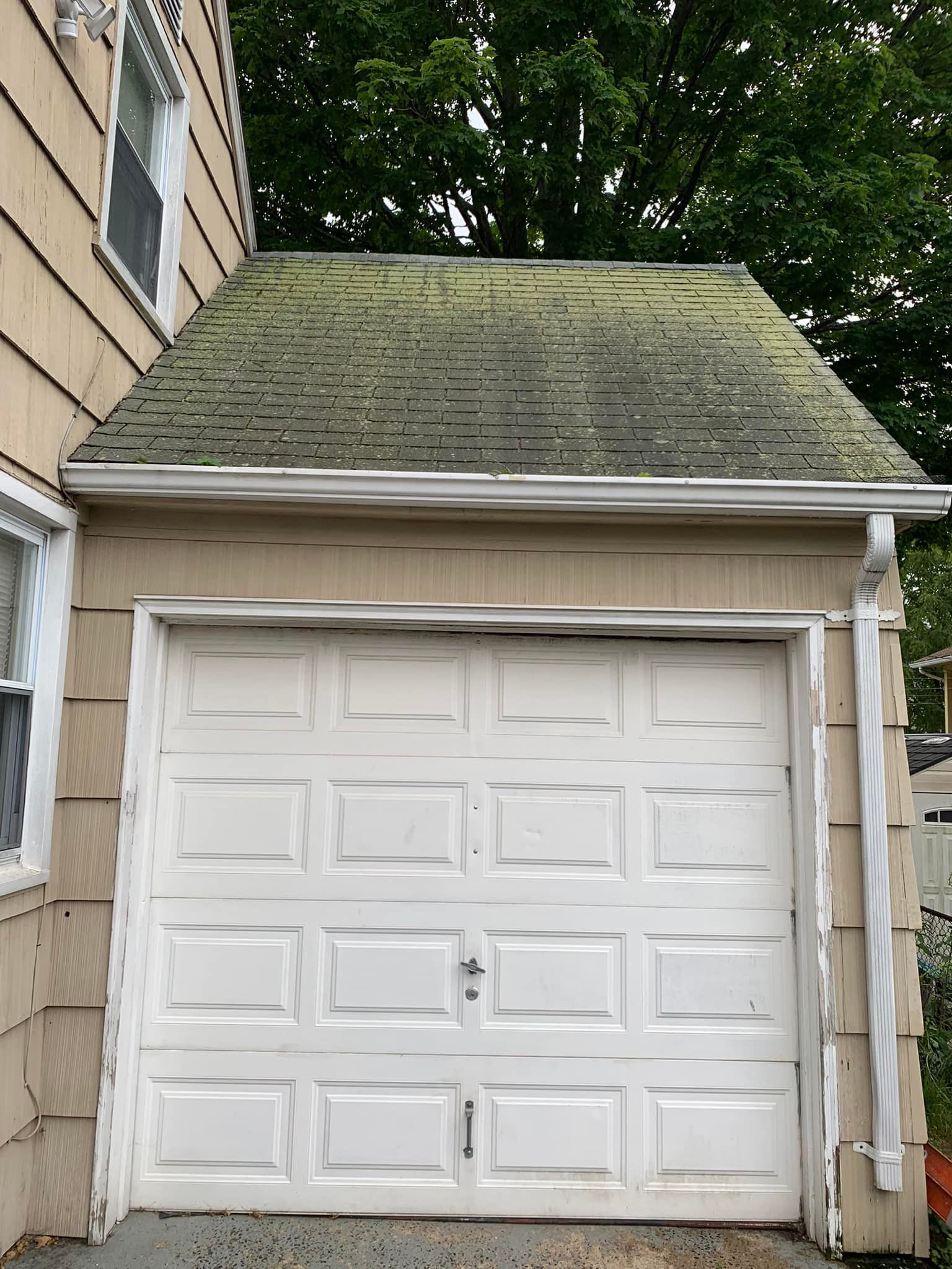 A white garage door with a green roof next to a house.