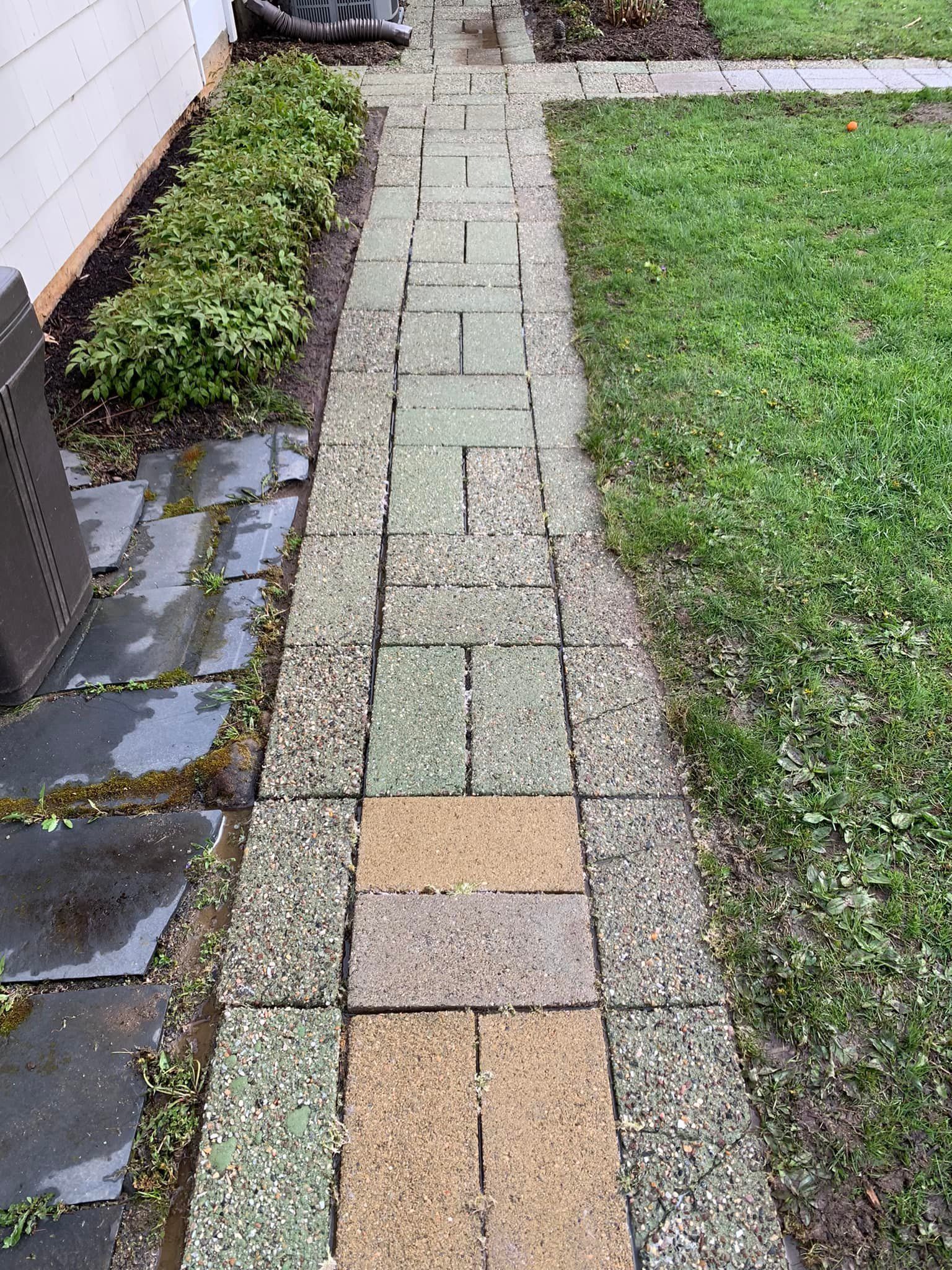 A brick walkway leading to a house next to a lush green lawn.