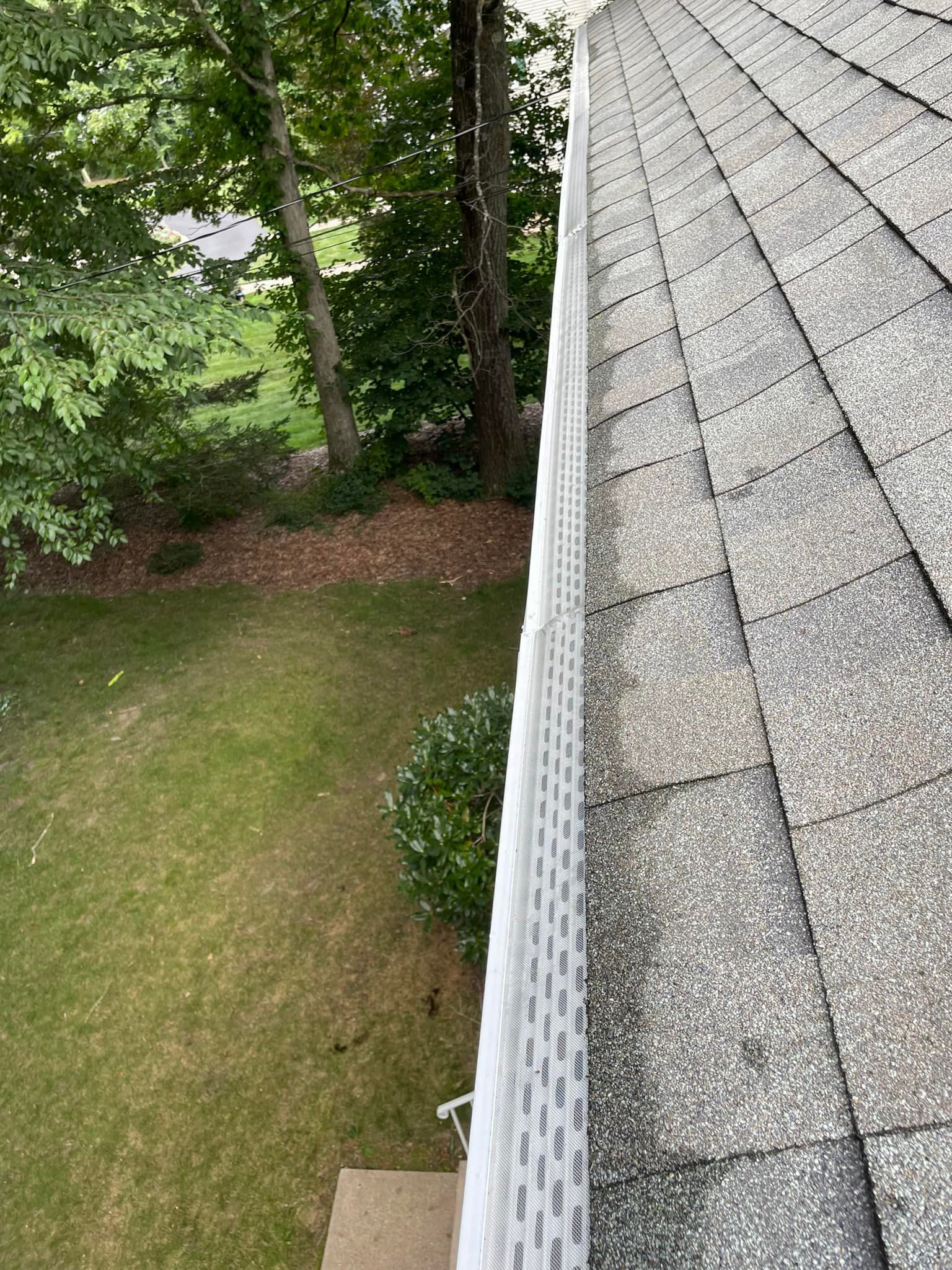 A gutter on the side of a house with trees in the background.