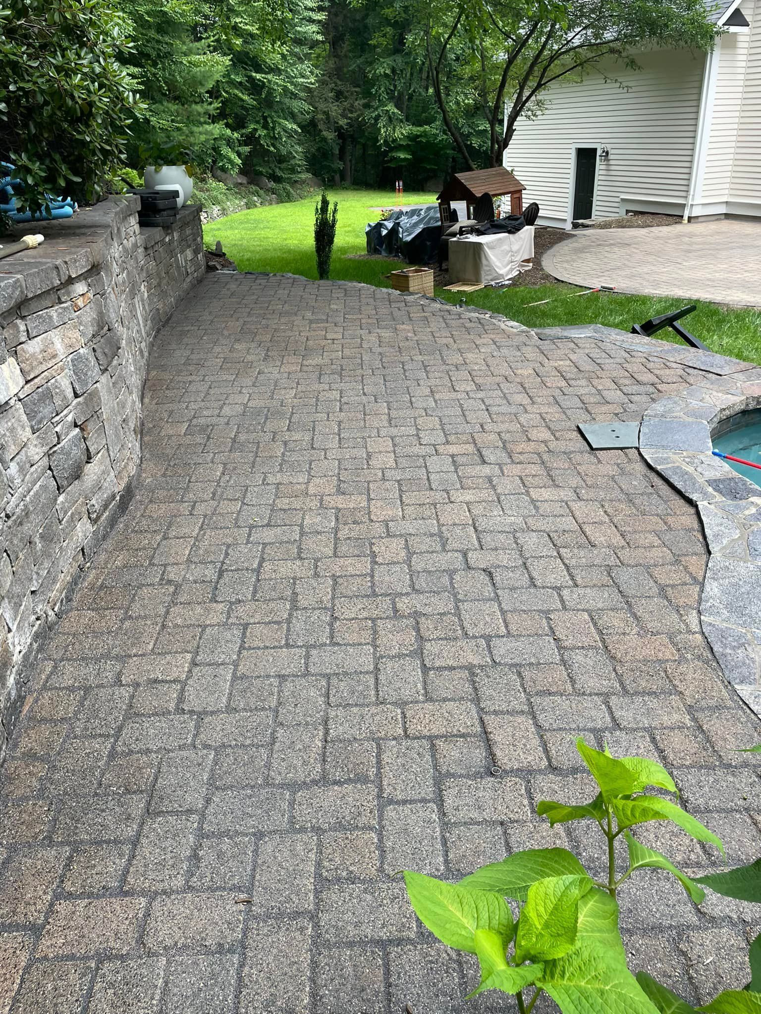 A brick walkway leading to a house with a pool in the backyard.