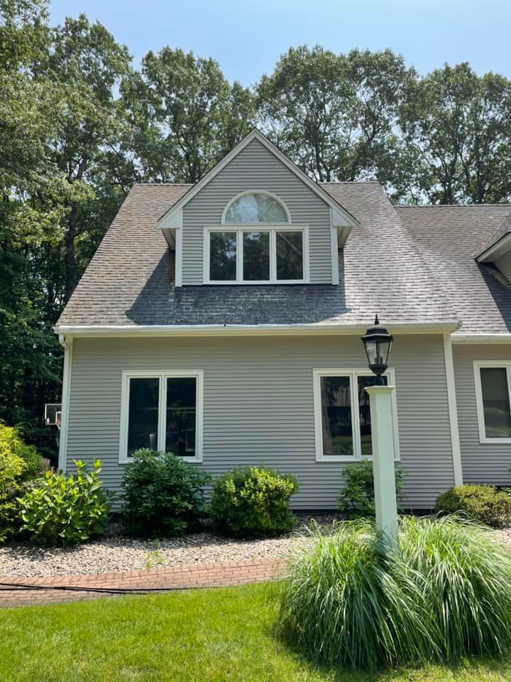 A large gray house with a gray roof and white trim is surrounded by trees.