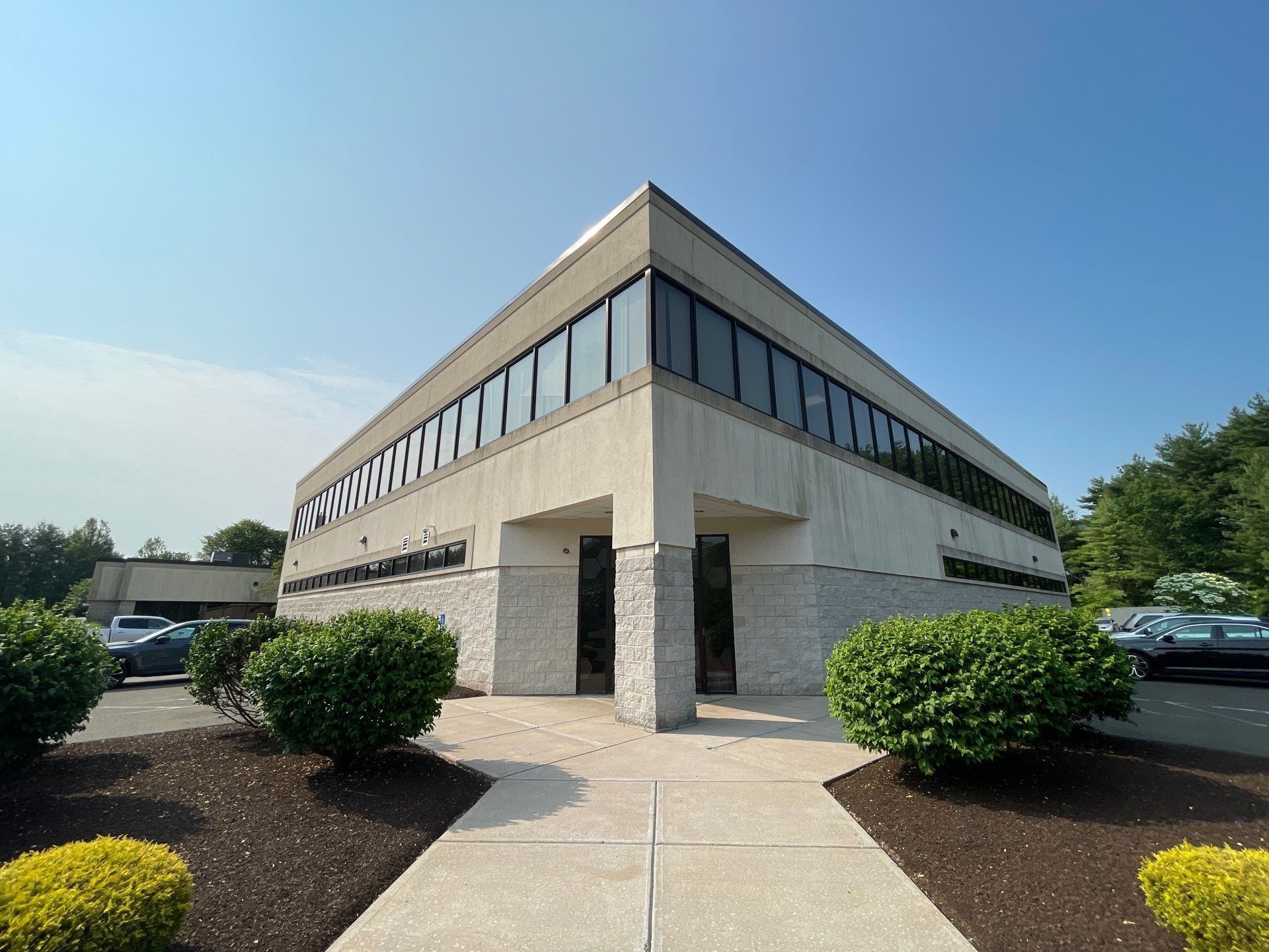 A large building with a lot of windows is surrounded by bushes and trees.