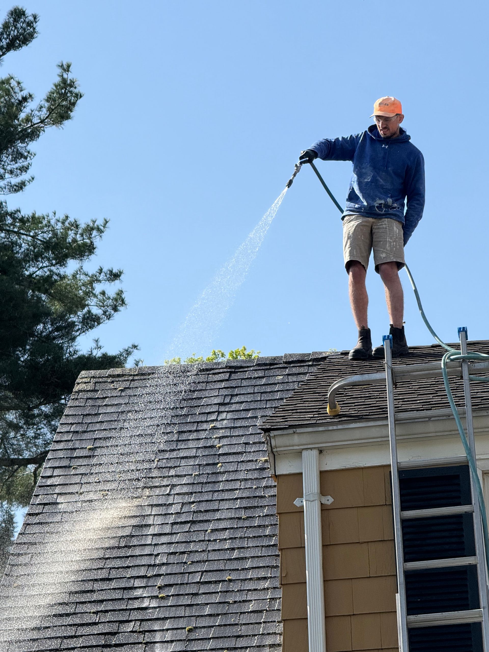 A man on a ladder spraying water on a roof