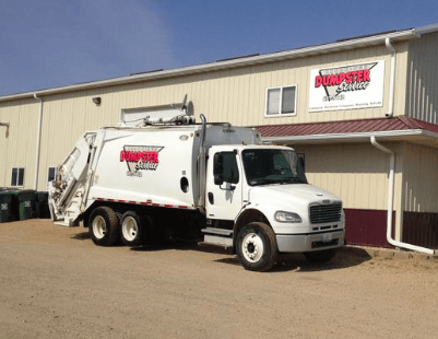 A dumpster truck is parked in front of a building