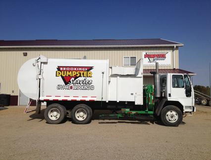 A white dumpster truck is parked in front of a building.