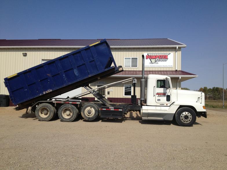 A dumpster truck is parked in front of a building