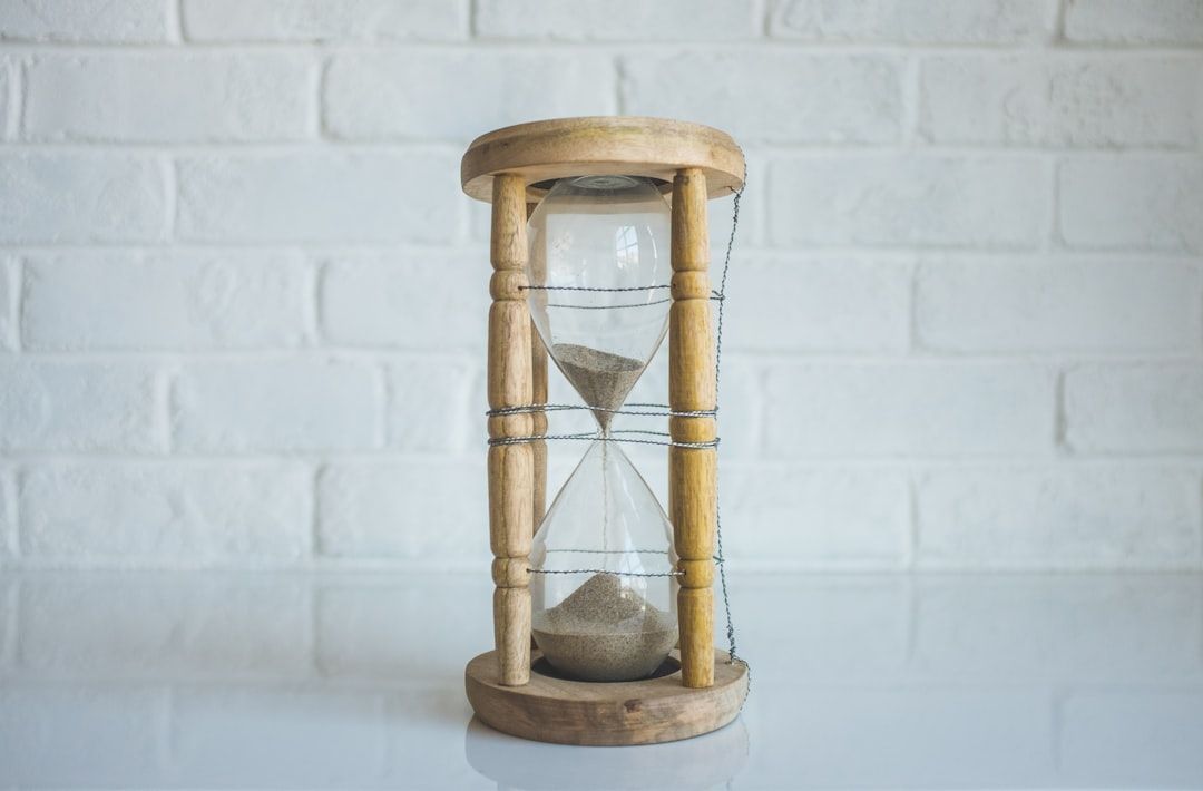A wooden hourglass is sitting on a white table in front of a white brick wall.