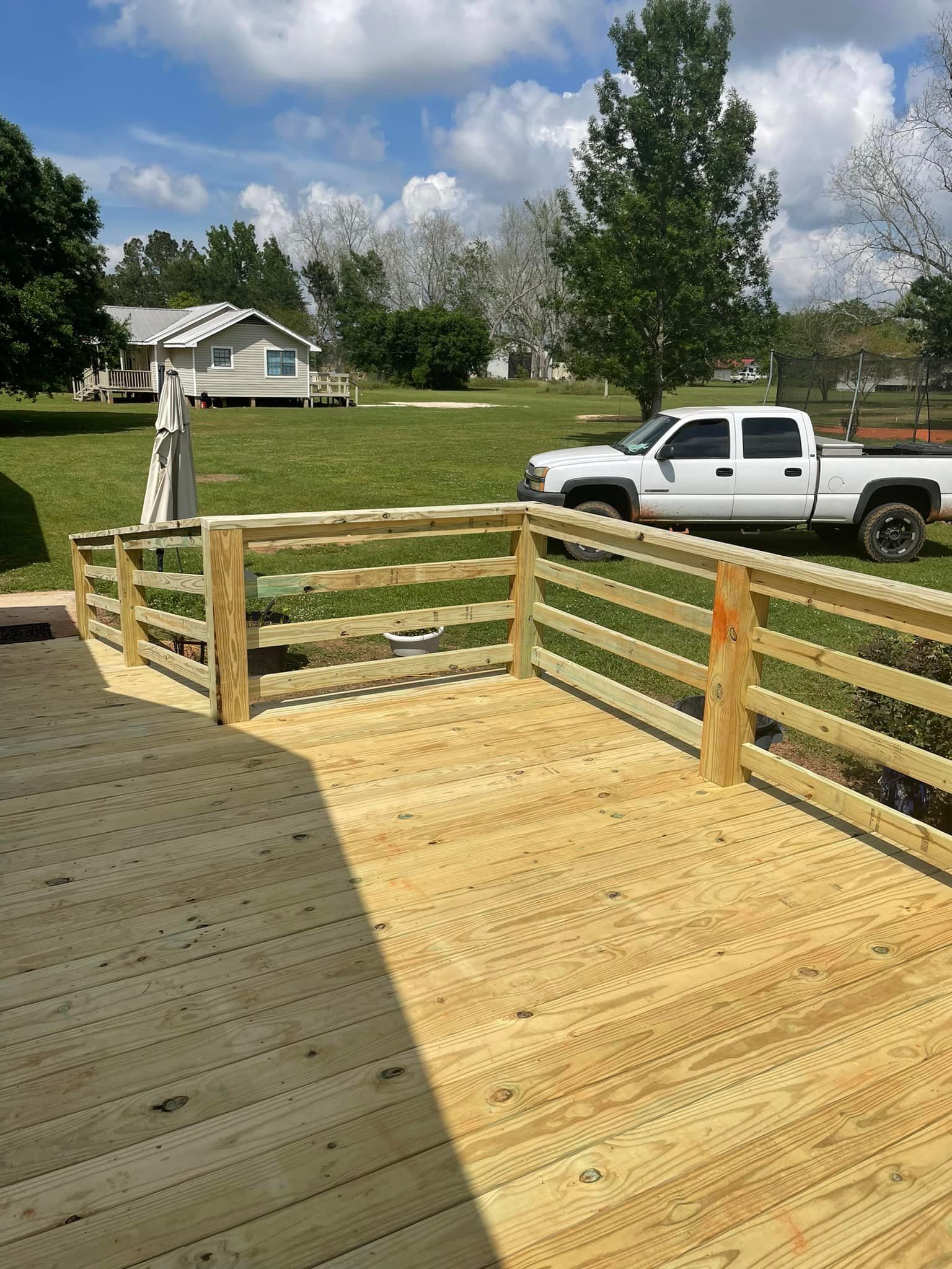 Wooden deck with railing, truck parked on grass, house in background, sunny day.